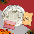 Raksha Bandhan set with silver pooja thali, colorful powders, Rakhi and a loving card, radiating tradition.