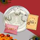 Artistic Rakhi collection featuring 9-inch silver thali, roli-chawal bowls, and a decorative festive card.